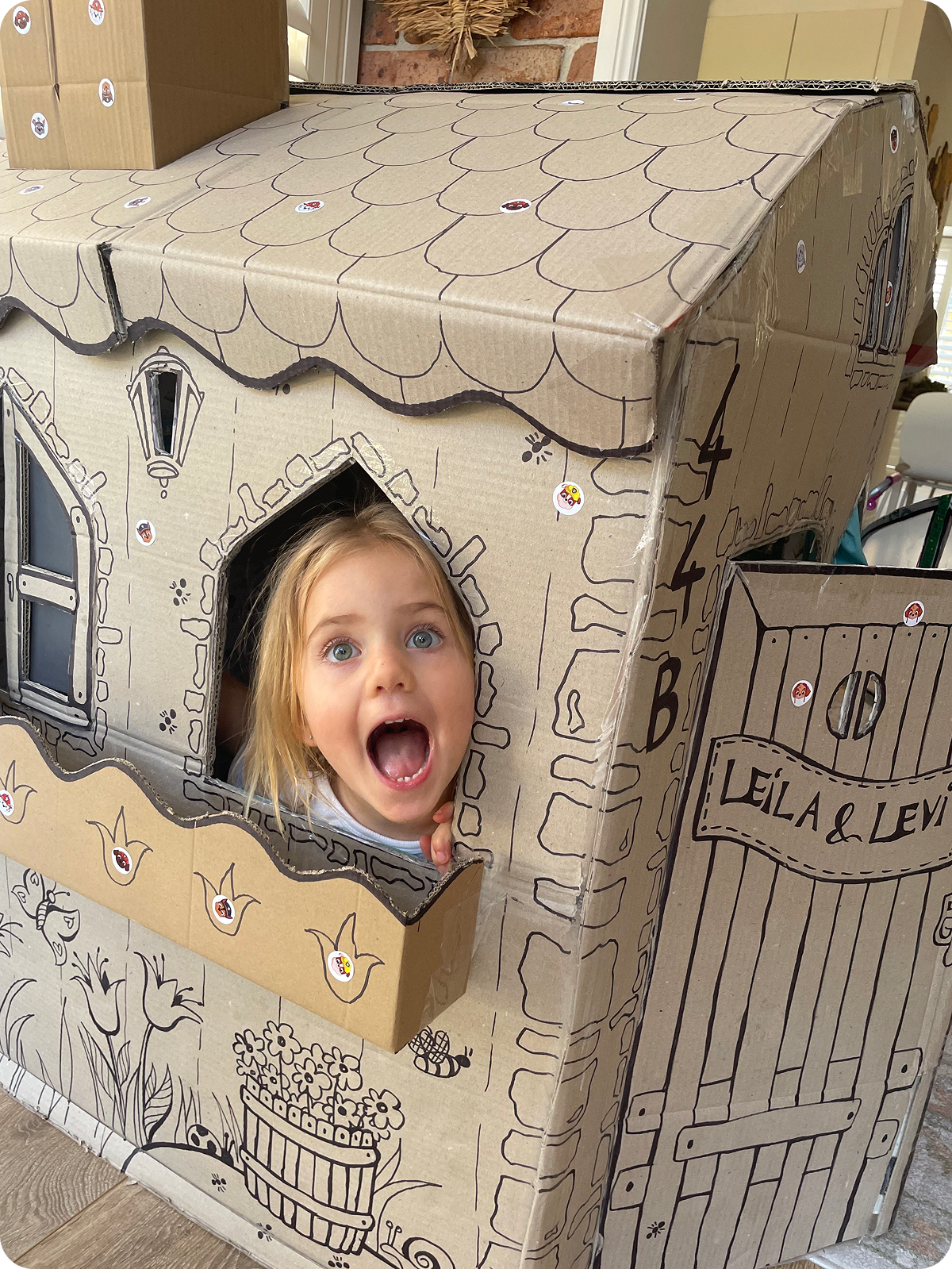 Child inside a hand-drawn cardboard playhouse